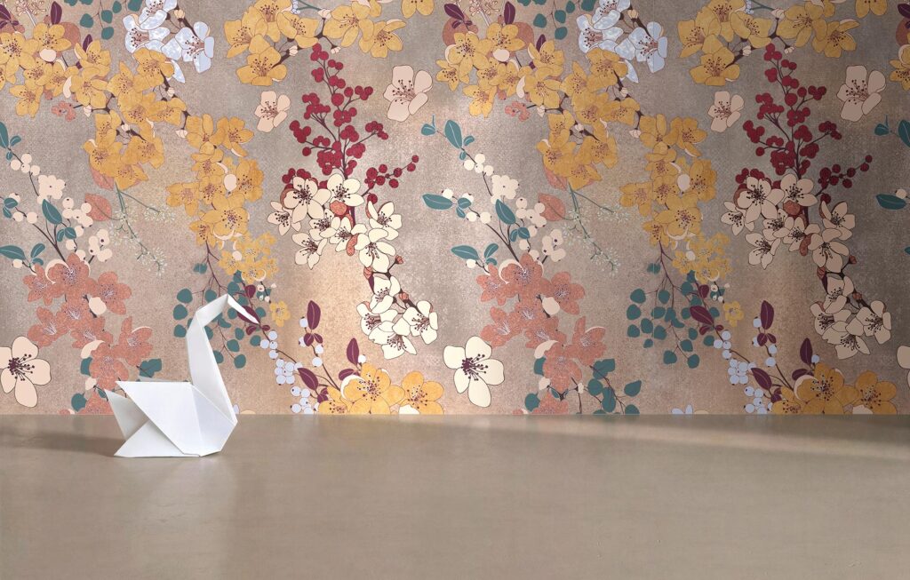 Collezione ART, rivestimento ceramico Decoro Petunia nel formato 60x120 cm. La parete presenta una posa a effetto carta da parati con un raffinato motivo floreale d'ispirazione orientale, caratterizzato da rami con fiori nei toni del giallo, rosa, bianco e rosso e foglie verdi su uno sfondo materico bronzo-dorato. In primo piano, su un pavimento continuo e liscio color tortora, è posizionato un delicato origami bianco a forma di cigno, lambito da una luce morbida che esalta l'atmosfera elegante, calda e minimalista dell'ambiente.