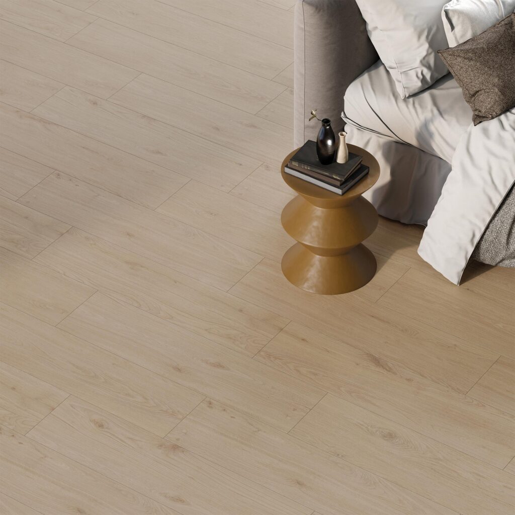 La collezione BARRIQUE, nella variante Almond Natural in formato 30x120 cm, definisce l'atmosfera calda e accogliente di questa camera da letto. Il pavimento in gres porcellanato effetto legno, caratterizzato da una posa sfalsata che esalta le venature e i nodi naturali del legno chiaro, fa da sfondo a un angolo notte elegante e moderno: si notano una porzione di letto con morbide lenzuola nei toni del bianco e del tortora e un comodino scultoreo in metallo dorato, su cui poggiano libri e vasi decorativi minimalisti.