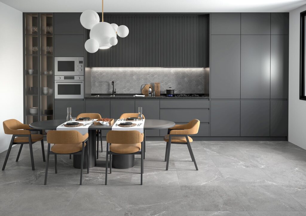 Collezione BLEND in gres porcellanato color Rock nell'elegante formato 60x60 cm, posata a pavimento in una cucina moderna e di design. Le piastrelle grigie effetto pietra valorizzano l'ambiente sofisticato, arredato con un'ampia cucina lineare grigio scuro opaco, un paraschizzi coordinato a mosaico esagonale e un tavolo da pranzo apparecchiato con poltroncine color senape. Un moderno lampadario a sfere bianche illumina l'intera stanza, creando un'atmosfera calda e accogliente.