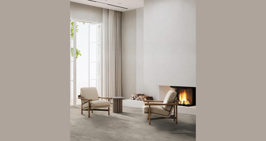La collezione BLEND, nella sfumatura calda Tan e formato 60x90 cm, definisce l'atmosfera elegante e accogliente di un moderno soggiorno. Il pavimento in gres porcellanato effetto pietra, caratterizzato da delicate venature naturali, è posato in un ampio spazio living luminoso e minimale. L'ambiente è valorizzato da due raffinate poltrone di design con struttura in legno e seduta chiara, un tavolino coordinato e un moderno camino a parete acceso che infonde una sensazione di calore e comfort.