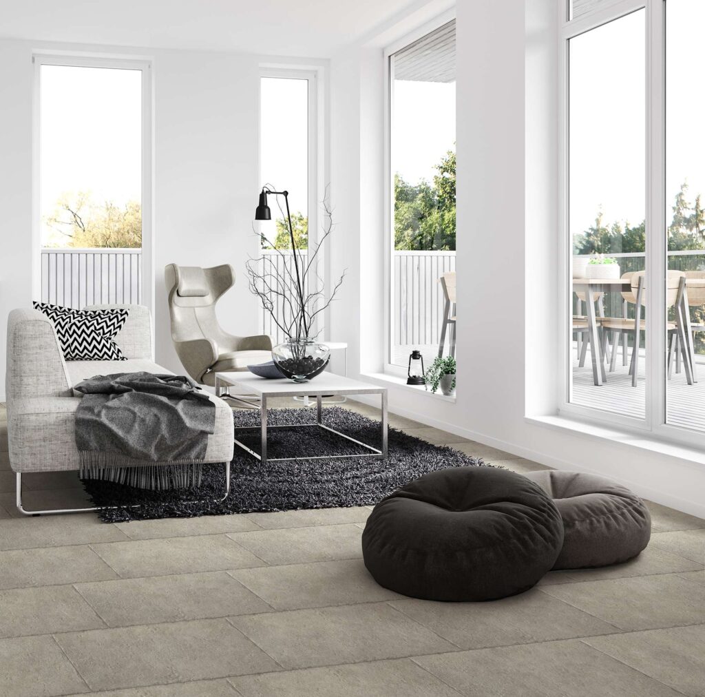 La collezione Bonnieux Pierre nel formato 30x60 definisce lo stile di questo luminoso soggiorno con un pavimento in gres porcellanato effetto pietra nelle calde sfumature del beige e del grigio chiaro. Le piastrelle, posate con schema sfalsato, si integrano perfettamente in un ambiente living moderno e sofisticato, caratterizzato da ampie vetrate, una raffinata chaise longue chiara, un tavolino da caffè minimalista e due morbidi pouf a sacco adagiati in primo piano, che completano un'atmosfera accogliente e di design.