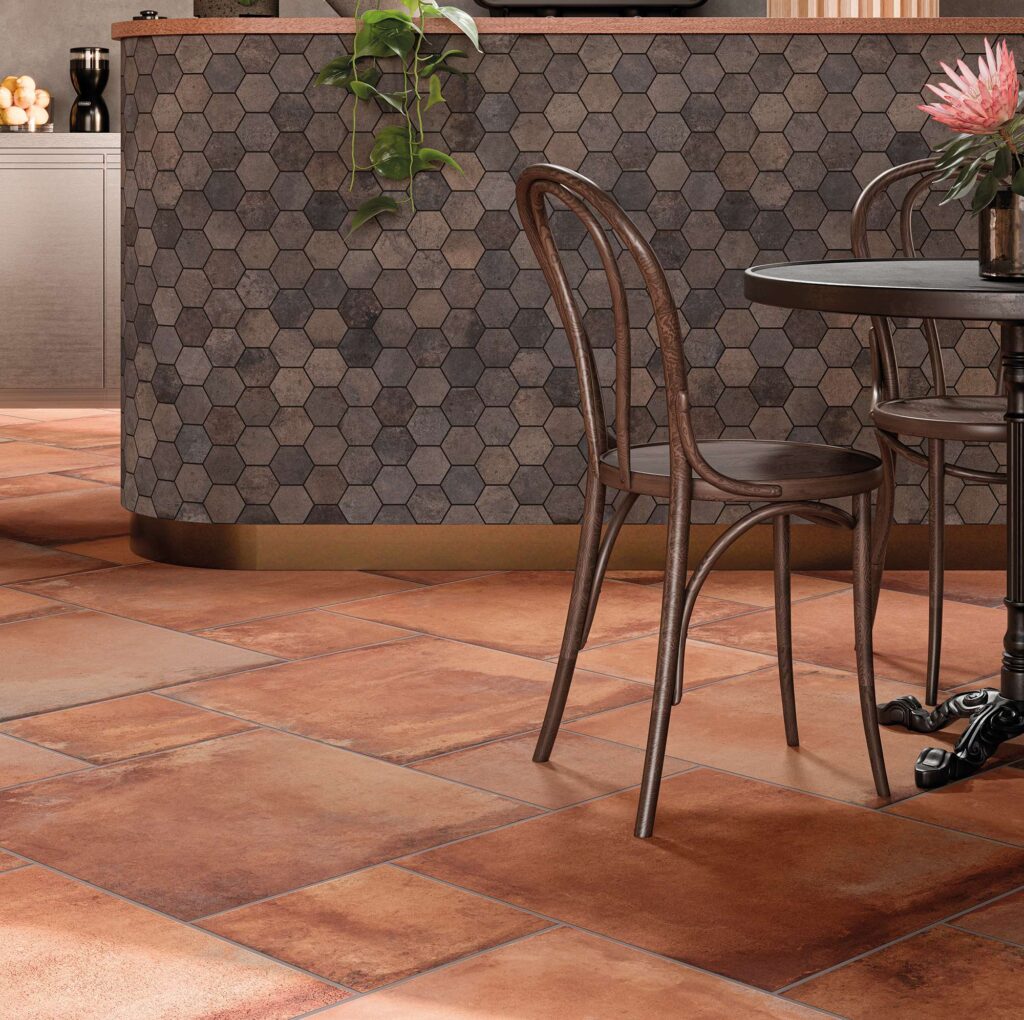 La collezione HEARTLAND in gres porcellanato color Terracotta, posata in multiformato, dona calore e naturalezza al pavimento di questo raffinato ristorante. Sullo sfondo, il bancone bar curvilineo è impreziosito dal rivestimento in mosaico esagonale Charcoal nei toni del grigio scuro antracite, abbinato a eleganti sedie in legno scuro in stile bistrot per un'atmosfera accogliente e di design.