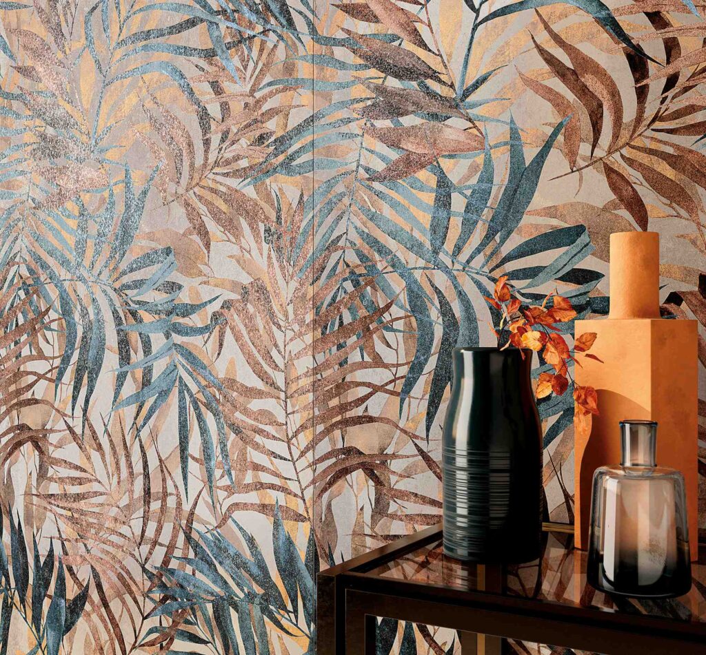 La collezione HEMISPHERE, nella variante decorata Dec. Savage Steel formato 60x120 cm con finitura lappata, si mostra in una raffinata posa a parete caratterizzata da un suggestivo pattern botanico con grandi foglie tropicali nei toni del blu metallico, bronzo e oro cangiante. In primo piano, un elegante tavolino da salotto ospita vasi ornamentali dal design contemporaneo nei toni caldi della terracotta e del nero, che richiamano i dettagli del rivestimento creando un'atmosfera d'interni lussuosa e accogliente.