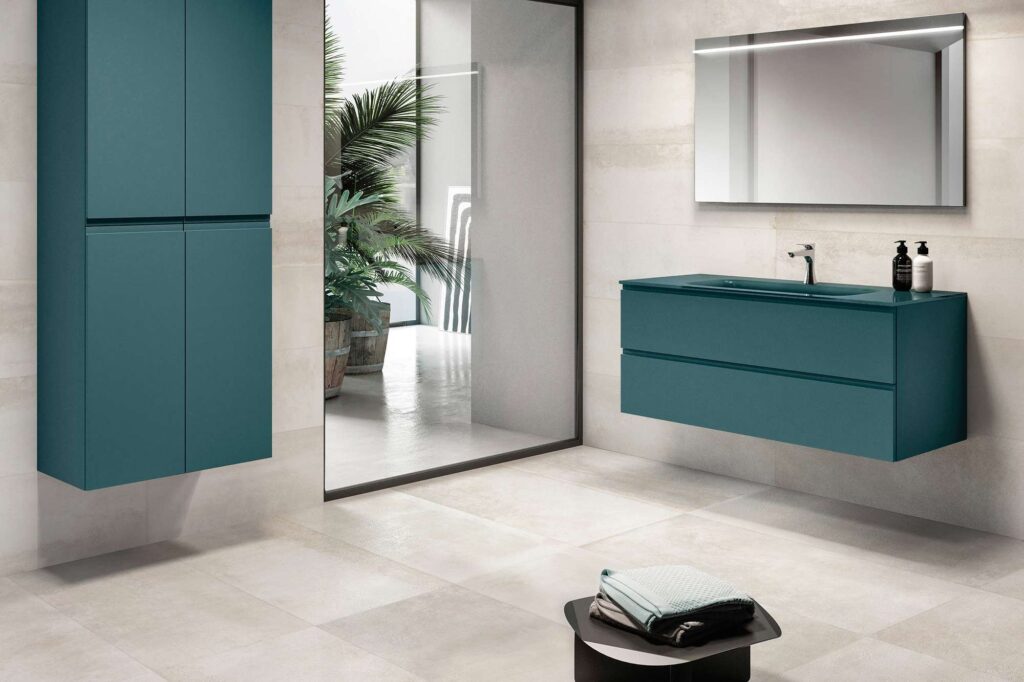 La collezione Hemisphere colore Platinum nel formato 60x120 riveste con eleganza le pareti e il pavimento di questo bagno dal design contemporaneo e minimale. Le grandi lastre in gres porcellanato, caratterizzate da una sofisticata tonalità chiara e luminosa con sfumature materiche, si abbinano armoniosamente a un arredo bagno sospeso color blu petrolio e a uno specchio lineare retroilluminato. La posa continua delle piastrelle amplifica la percezione dello spazio, arricchito sullo sfondo da un'ampia vetrata con vista su rigogliose piante verdi che donano freschezza all'ambiente.