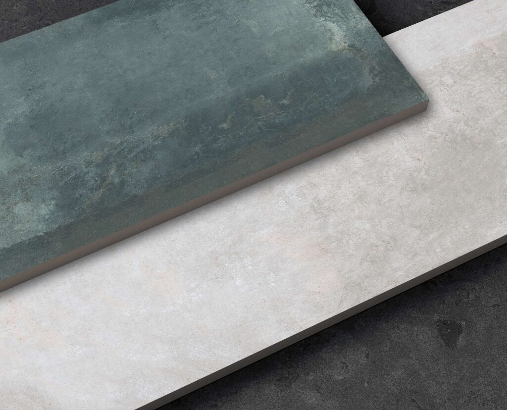Collezione HEMISPHERE: un raffinato render che valorizza il concetto "Double Surface" attraverso due grandi lastre ceramiche rettangolari, sovrapposte diagonalmente su uno sfondo materico scuro. La lastra superiore si distingue per una profonda tonalità verde petrolio con sfumature naturali e finitura leggermente vissuta, mentre quella inferiore presenta una superficie grigio chiaro/off-white effetto pietra fine. Una composizione d'impatto che mette in risalto la qualità dei dettagli, le texture tattili e l'eleganza contemporanea dei formati ceramici d'eccellenza.