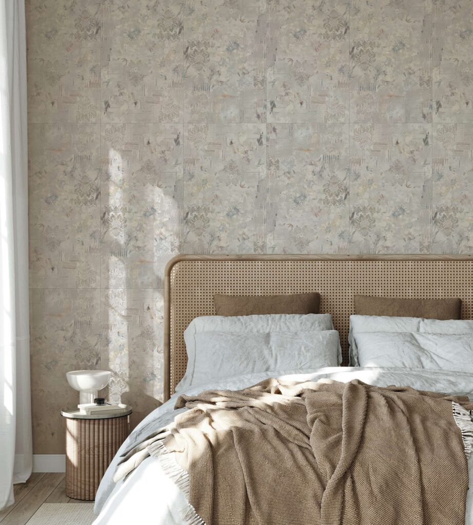 La collezione I presenta il decoro Boheme nel formato 60x120 cm, utilizzato come raffinato rivestimento a parete con posa verticale in una camera da letto dal design contemporaneo e accogliente. Le piastrelle in gres porcellanato sono caratterizzate da una texture artistica d'ispirazione vintage con delicati motivi floreali e damascati, sfumati in tonalità neutre del beige, grigio e tocchi pastello. La parete decorata fa da sfondo a un letto elegante con testiera in paglia di Vienna, arricchito da tessili morbidi e un copriletto color nocciola, il tutto valorizzato da una lama di luce naturale che attraversa la stanza creando un'atmosfera calda, luminosa e rilassante.