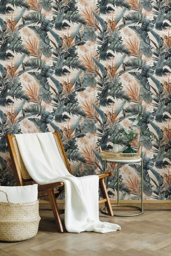 La collezione I Decors, con il decoro Proton Texdeco Warm nel formato 60x120, veste la parete ricreando un suggestivo effetto carta da parati a tema tropicale, caratterizzato da grandi foglie di palma nei toni del verde foresta e del ruggine caldo. L'ambiente, intimo e accogliente, è arredato in stile naturale con una sedia in legno e paglia di Vienna impreziosita da una morbida coperta bianca, un cesto in vimini e un elegante tavolino circolare con rami di eucalipto, il tutto valorizzato da un raffinato pavimento in parquet a spina di pesce.