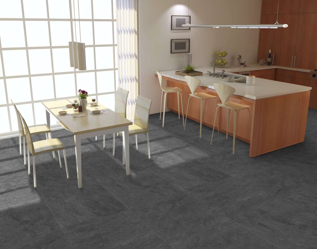 La collezione Jelling Titanium nel formato 60x60 cm veste con eleganza il pavimento di questa moderna e luminosa cucina open space. Le piastrelle in gres porcellanato nei toni del grigio scuro effetto pietra, posate in modo regolare, creano una superficie continua e materica. Sulla sinistra, un tavolo da pranzo in legno chiaro con quattro sedie è posizionato accanto a una grande vetrata a riquadri che inonda la stanza di luce naturale; sulla destra trova spazio un'isola cucina in legno con top bianco e tre raffinati sgabelli di design, per un ambiente dal design contemporaneo e accogliente.