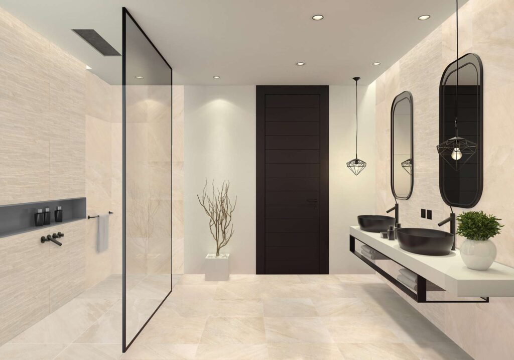 La collezione Ocean, qui presentata nella raffinata tonalità sabbia (Sand) nel formato 60x60 e nella variante decorativa a Muretto, riveste un bagno moderno dal design esclusivo. L'immagine mostra un ambiente luminoso caratterizzato dal contrasto armonioso tra le calde sfumature beige dei pavimenti e rivestimenti effetto pietra e gli eleganti dettagli neri (black): la porta opaca sullo sfondo, i due lavabi da appoggio con specchi ovali coordinati e il profilo minimalista della doccia walk-in con cristallo trasparente. Un'ispirazione d'eccellenza per un bagno contemporaneo, accogliente e di grande impatto visivo.