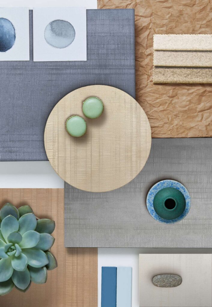 La collezione ORGANIC si svela in una sofisticata moodboard di design che accosta campioni ceramici d'eccellenza con una raffinata texture effetto tessuto ("Rug") in sfumature naturali di grigio, blu ardesia, beige dorato e terracotta. Questa vista dall'alto (flat lay) cattura un'atmosfera armoniosa e materica, in cui le superfici ceramiche dai diversi formati geometrici – rettangolari e circolari – dialogano con dettagli decorativi naturali: una pianta succulenta, macarons verdi, un piccolo vaso in ceramica smaltata e campioni di colore coordinati, evocando un'eleganza contemporanea e organica.