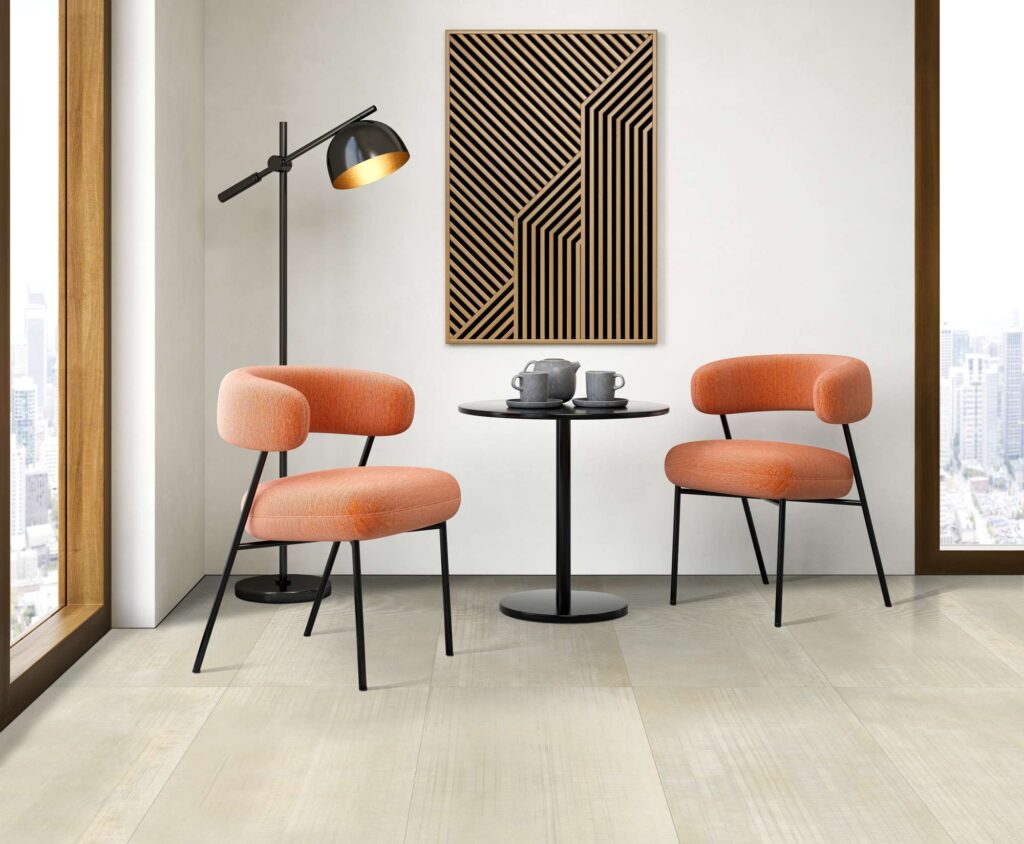 Collezione Organic, tonalità Sand: pavimento in gres porcellanato di grande formato in un ambiente living o lounge dal design moderno e raffinato. L'elegante spazio è arredato con due poltroncine color pesca con gambe metalliche nere, disposte ai lati di un tavolino nero con un set da tè. Una lampada di design e un quadro geometrico in legno decorano la stanza, caratterizzata da ampie finestre che offrono una luminosa vista sullo skyline della città.