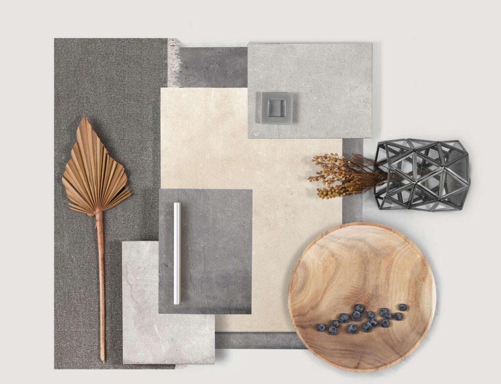 Collezione UNIKA: un raffinato moodboard in stile flat lay che presenta campioni di piastrelle in gres porcellanato nei toni caldi del beige e in varie sfumature di grigio effetto pietra. La composizione, pensata per l'interior design d'eccellenza, accosta le superfici ceramiche a elementi d'arredo e texture naturali, tra cui una foglia di palma secca, un piatto in legno con mirtilli, un vaso geometrico in metallo e vetro con rami fioriti, e dettagli di maniglie moderne.