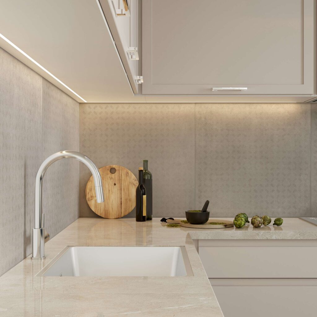 La collezione XO Poudre Grid nel formato 60x60 riveste con eleganza il backsplash di questa cucina moderna e raffinata. Nel primo piano, le piastrelle ceramiche nei toni del grigio caldo e cipria (poudre) mostrano una delicata texture a griglia geometrica, splendidamente illuminata da una barra LED sottopensile. Sul top in marmo beige, accanto a un lavello di design con miscelatore cromato, sono disposti con cura un tagliere in legno rotondo, bottiglie d'olio, un mortaio e alcuni carciofi freschi, evocando un'atmosfera calda e accogliente.