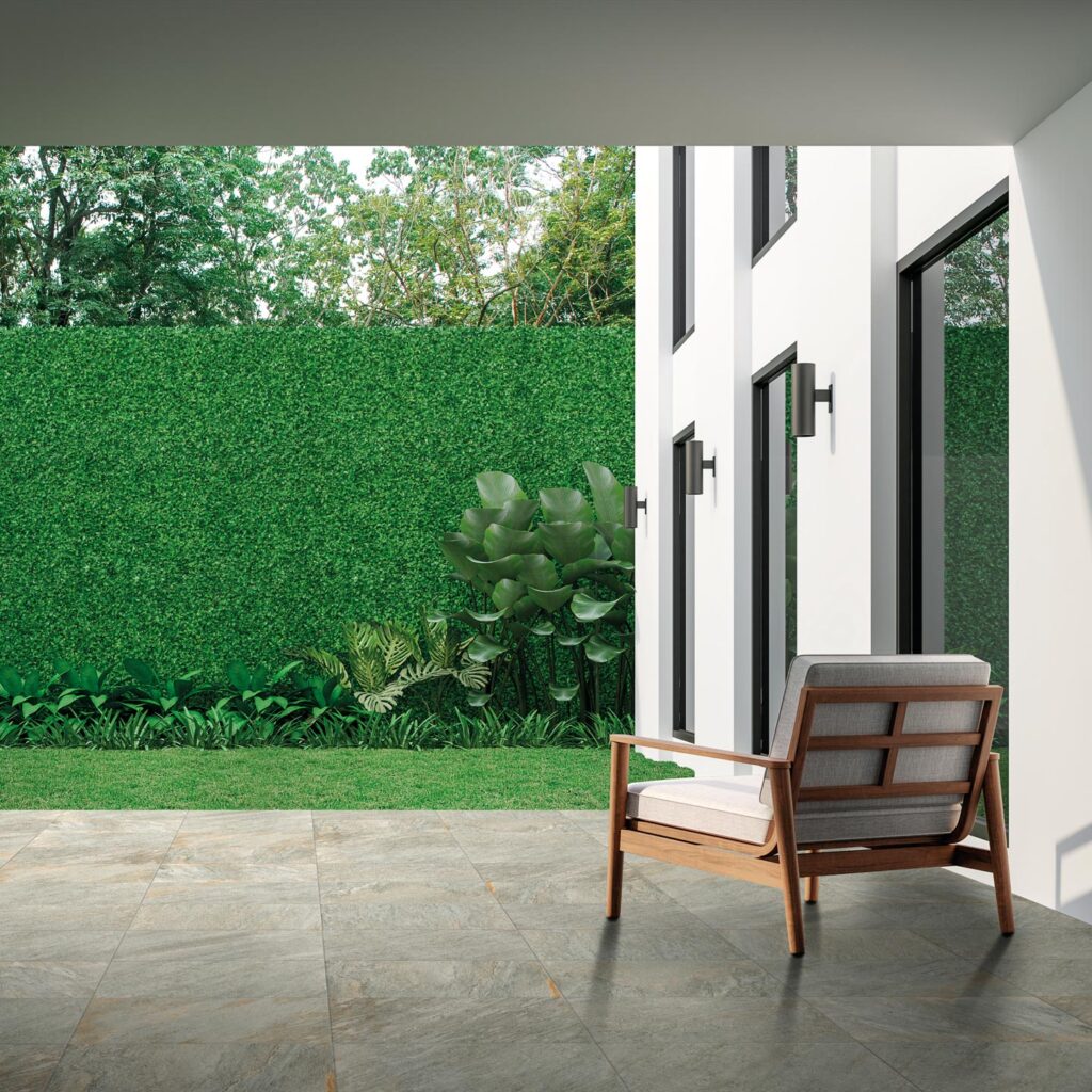 Collezione Seattle Grigio per esterni, utilizzata per la pavimentazione con posa a correre di un portico. Il gres porcellanato effetto pietra grigia dona eleganza e continuità visiva all'ambiente outdoor, impreziosito da lettini prendisole moderni e ampie vetrate di una villa signorile.