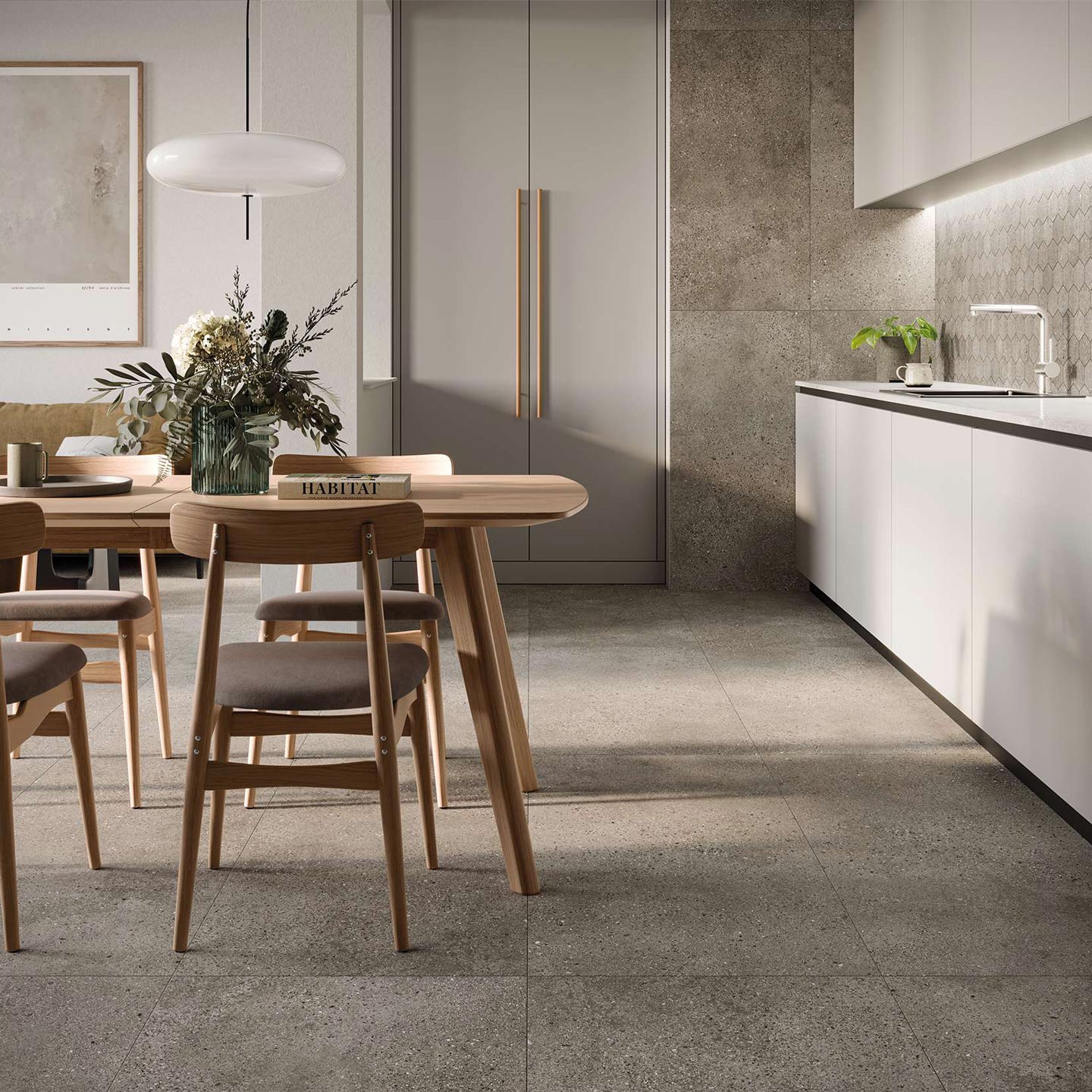 La collezione Mon Greige in gres porcellanato effetto pietra arreda una cucina moderna e luminosa, con pavimenti e rivestimenti verticali nel formato 60x120 cm nella calda tonalità greige. Sullo sfondo, la zona lavoro con mobili bianchi minimalisti è valorizzata dal paraschizzi in mosaico esagonale coordinato (Mos. Esagona). Sulla sinistra, la zona pranzo presenta un tavolo e sedie in legno chiaro, definendo un'atmosfera calda, elegante e contemporanea, esaltata dalla luce naturale che mette in risalto la raffinata matericità delle superfici ceramiche.